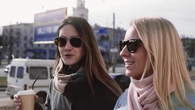 慢动作。两个白人女性谈话。20多岁的女士穿着时髦的衣服和太阳镜在街上微笑
