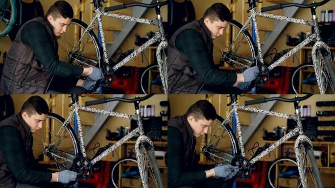 熟练的年轻人专业机械师正在修理自行车踏板，钥匙坐在他工作场所地板上的自行车附近。维护、工具和人的概念