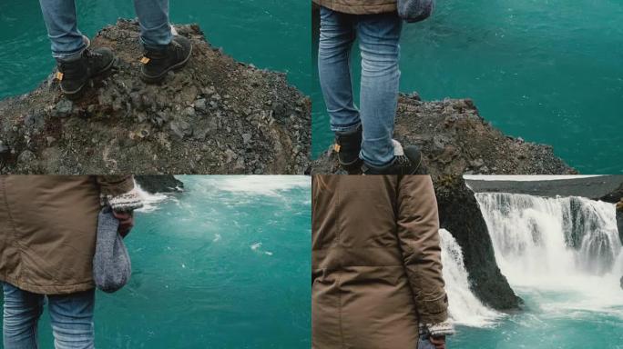 年轻女子站在冰岛一个强大的瀑布附近的岩石上，看着落下的水流