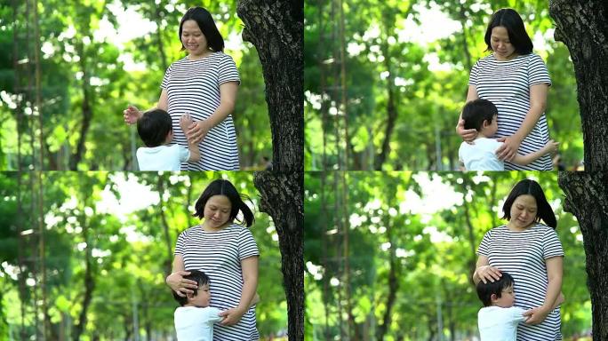 有孩子在户外的孕妇。夏天公园里自然背景的母子俩。抱着母亲的小男孩，第二次怀孕。怀孕，新生活，家庭，父