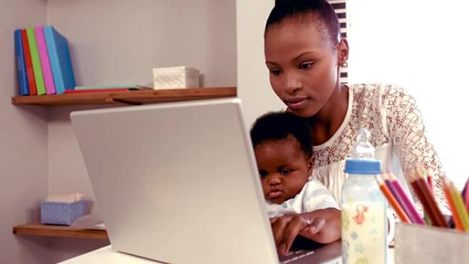 带着婴儿在键盘上打字的微笑妈妈