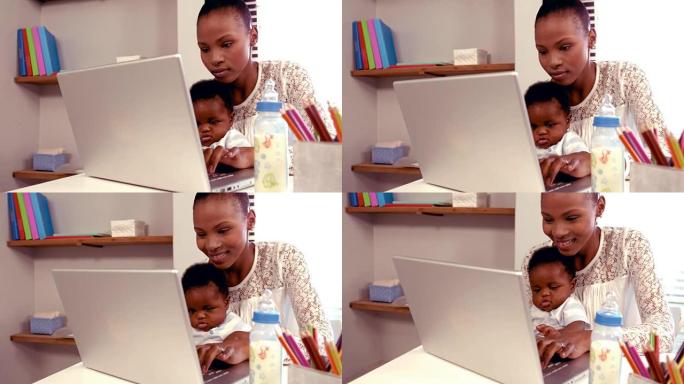 带着婴儿在键盘上打字的微笑妈妈