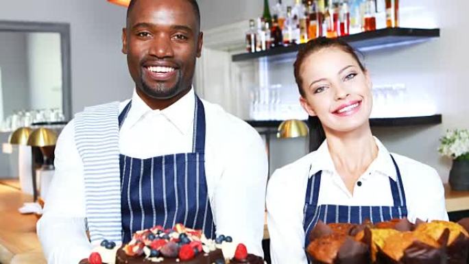 微笑的服务员和女服务员在柜台上展示甜点的肖像