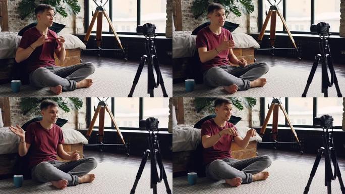 穿着休闲服装的帅哥博客作者正在用专业相机在家为他的互联网vlog录制视频，他正在与订阅者交谈，打手势
