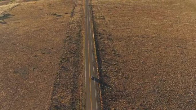 空中: 在日落时沿着空旷的乡村道路行驶的SUV汽车上方飞行