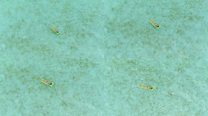 航拍:年轻女子穿着泳衣躺在充气床垫上，漂浮在梦幻般的博拉博拉岛清澈的海面上