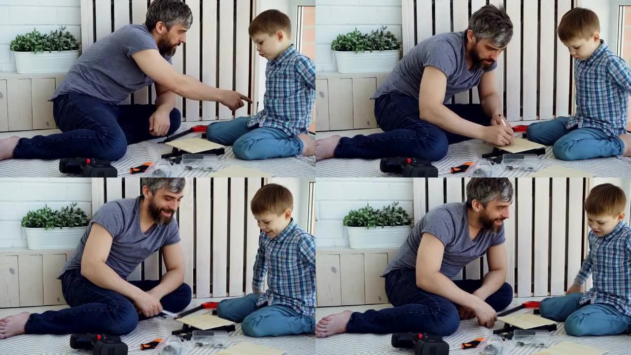 友好的父亲和小儿子坐在家里做建筑工作时有说有笑。对话、工具和为人父母的概念。
