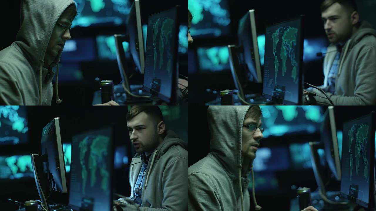 两名穿着连帽衫的黑客在一台电脑上工作，电脑上有地图和数据显示在黑暗的办公室里。