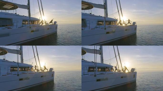 三个美丽健康的女人在一艘白色帆船双体船上做早晨瑜伽的航拍。平静的大海，太阳升起，平静的大海。