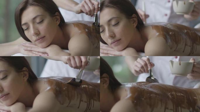 年轻的黑发女人正在健康中心接受放松的巧克力按摩治疗。