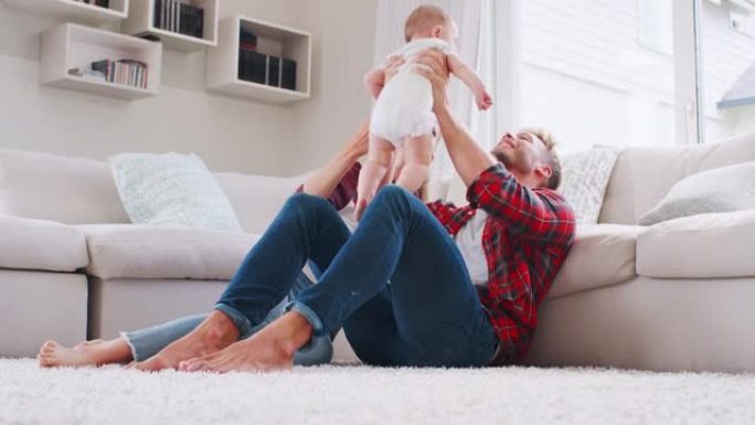 年轻的白人夫妇坐在家里举起婴儿，低角度
