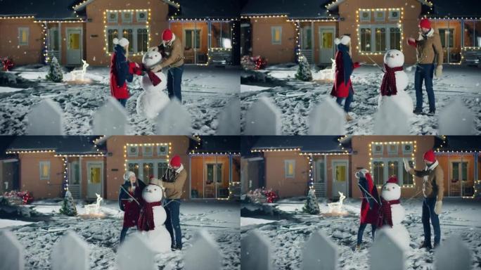 幸福的年轻夫妇在下雪的时候在他们田园诗般的房子的后院堆雪人。他们用围巾包裹雪人。家人在平安夜共度时光