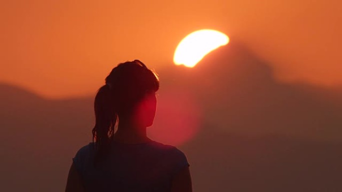 年轻女子用双手在山后美丽的金色太阳下使心