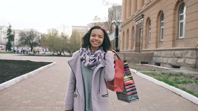 多莉拍摄了迷人的混血女孩带着购物袋走向，对着镜头微笑。快乐的年轻女子在逛商场后散步