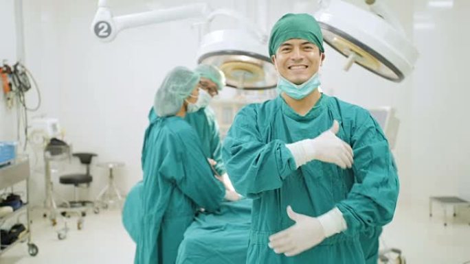 高加索男性外科医生的肖像穿着完整的手术磨砂膏微笑着相机，团队医生在医院手术室为病人做手术。