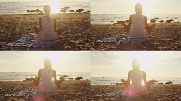 年轻的金发女孩在日落的沙滩上冥想荷花姿势