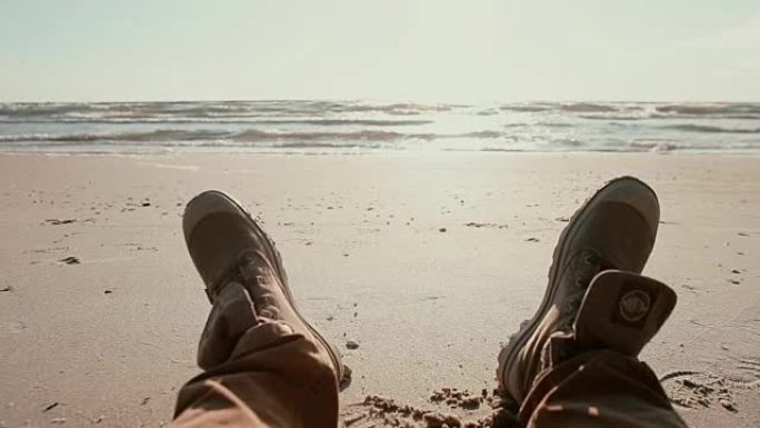 一个躺在沙滩上欣赏水景的人的靴子特写