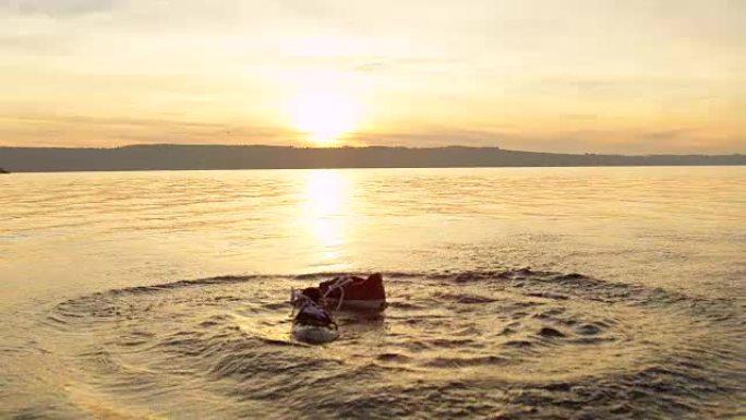 慢动作: 金色日落时，鞋子掉入水中并漂浮在水面上