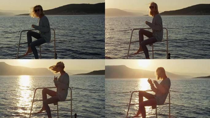美丽的年轻女子坐在游艇甲板上看日落和海景时，松开了金色的头发。