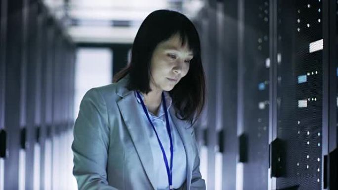 亚洲女性IT工程师工作在一个应急车笔记本电脑，她扫描硬盘。她在满是机架服务器的大数据中心。