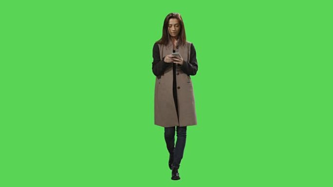 休闲的黑发女性正在散步，并在背景的模拟绿屏上使用智能手机。