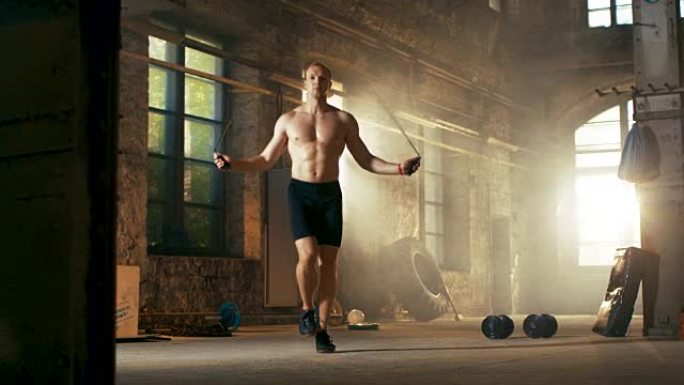 运动赤膊健美男子在一个废弃的工厂硬核健身房用跳绳锻炼。他从他的激烈健身训练中满身是汗。