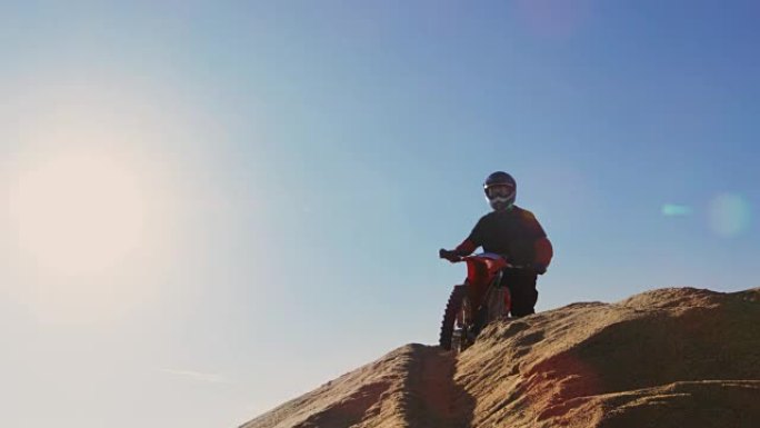 专业摩托车越野赛摩托车骑手在沙丘上驾驶和停车的低角度镜头。