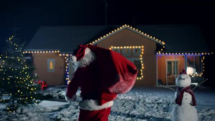 地道的圣诞老人肩上扛着红色的包，走进装饰着灯光和花环的田园诗般的房子的前院。圣诞老人带来礼物和礼物。