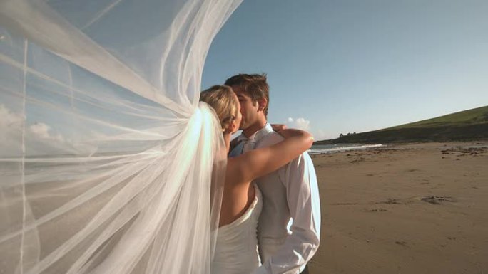 站在海滩上亲吻新娘夫妇