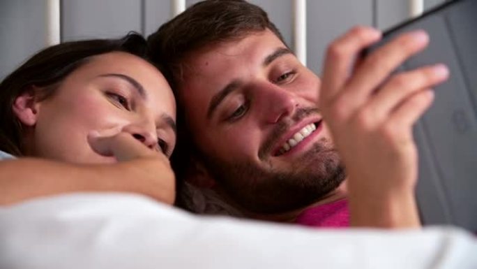 使用数字平板电脑躺在床上的年轻夫妇