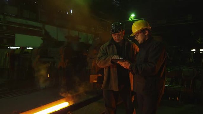 工程师和工人在铸造厂交谈。使用平板电脑的工程师。恶劣的工业环境。
