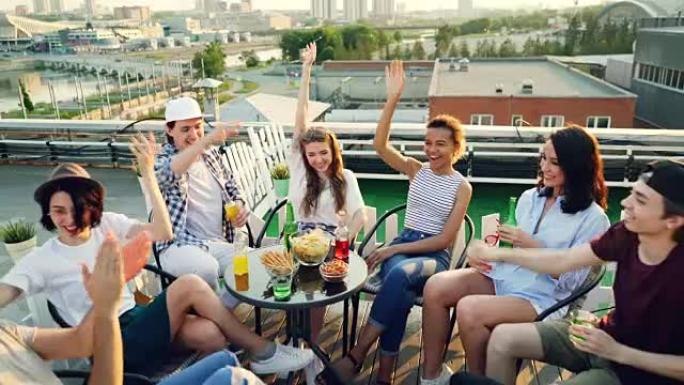 快乐的朋友们将双手放在一起，然后在空中坐在屋顶上的桌子上围成一圈喝酒。团结、聚会和庆祝理念。