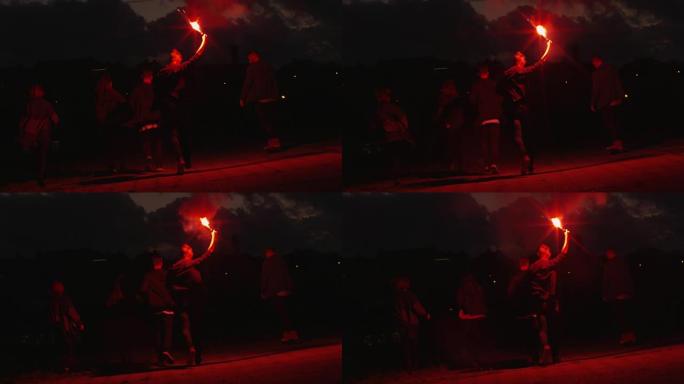 晚上，一群青少年手持并挥舞着红色信号弹，向摄像机外奔跑。
