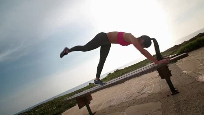 健康的女人在长凳上做腹肌和大腿锻炼