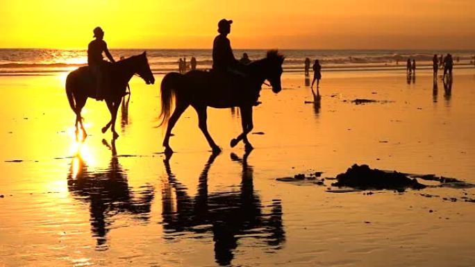 在梦幻般的库塔海滩上的慢动作游客在神奇的金色日落中骑马