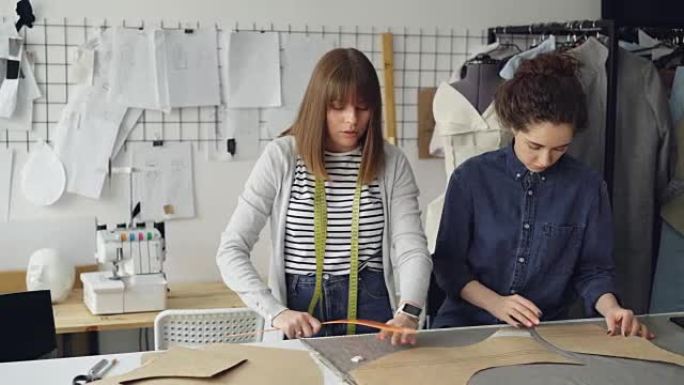 创意设计师团队正在裁缝店处理服装图案和面料。年轻女性专注于测量。背景缝纫项目和工具。