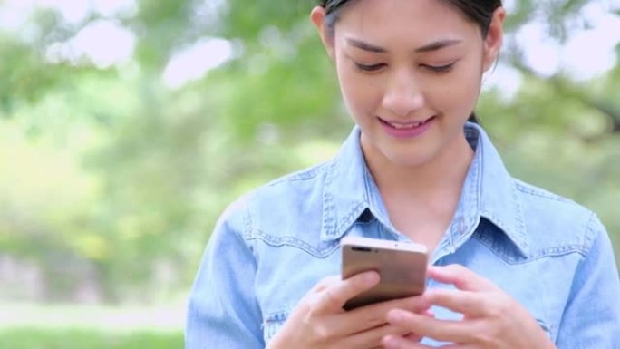 女性手在触摸屏智能手机上发短信或打字。年轻女子带着智能手机在公园散步。