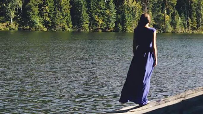 穿着长裙站在湖边岸边的美丽年轻女子的慢动作