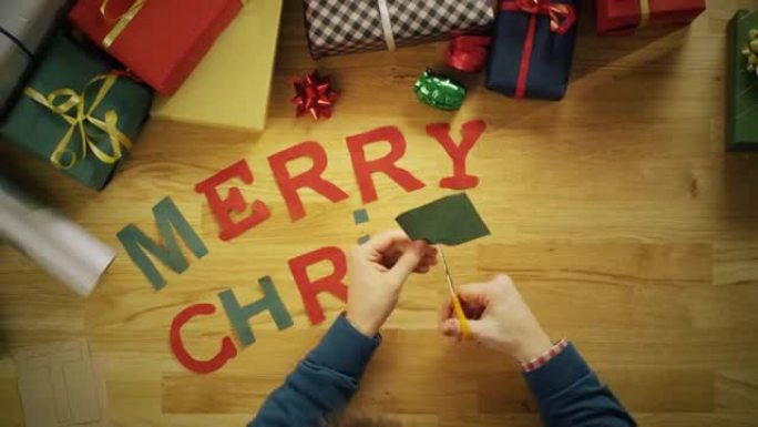 一名男子剪字母 “圣诞快乐”，并用礼品盒将其放在木桌上的俯视图延时。