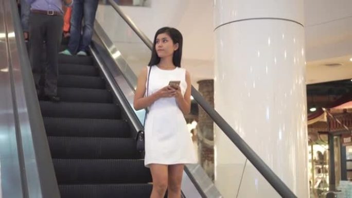 在购物中心的自动扶梯上使用智能手机的女人