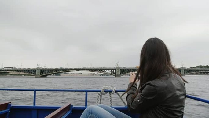 黑发女人在圣彼得堡的一座桥拍照。她坐在一辆河边的公共汽车上，风吹着她的头发，慢慢地