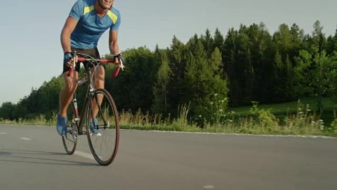 低角度: 年轻的男性骑自行车的人沿着空旷的柏油路踩踏板，经过相机。