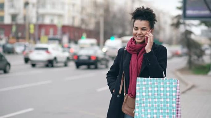 迷人的非洲裔美国妇女，带着购物袋在等出租车和从商场销售回来时打电话