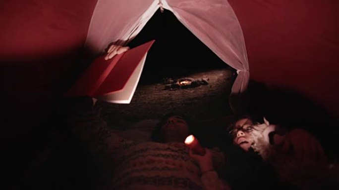 年轻的父子在露营帐篷里读睡前故事