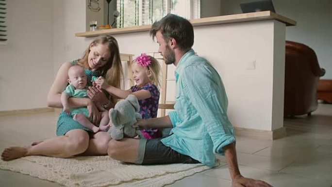 美丽的年轻家庭: 妈妈，爸爸，小女儿和宝贝儿子坐在厨房地板上。慢动作