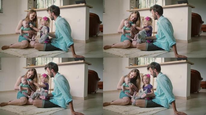 美丽的年轻家庭: 妈妈，爸爸，小女儿和宝贝儿子坐在厨房地板上。慢动作