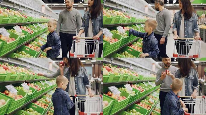 年轻的家庭妈妈，爸爸和小男孩正在超市里挑选水果，抚摸和闻到它们，并放入手推车。购买食物和人的概念。