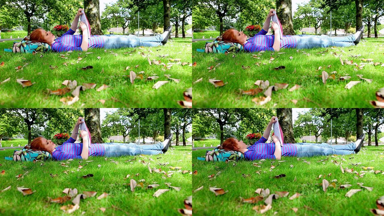 漂亮的年轻学生躺在草地上写作