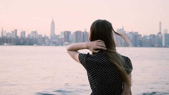 体贴的年轻高加索女孩，头发在风中吹，在纽约市河岸慢动作观看日落