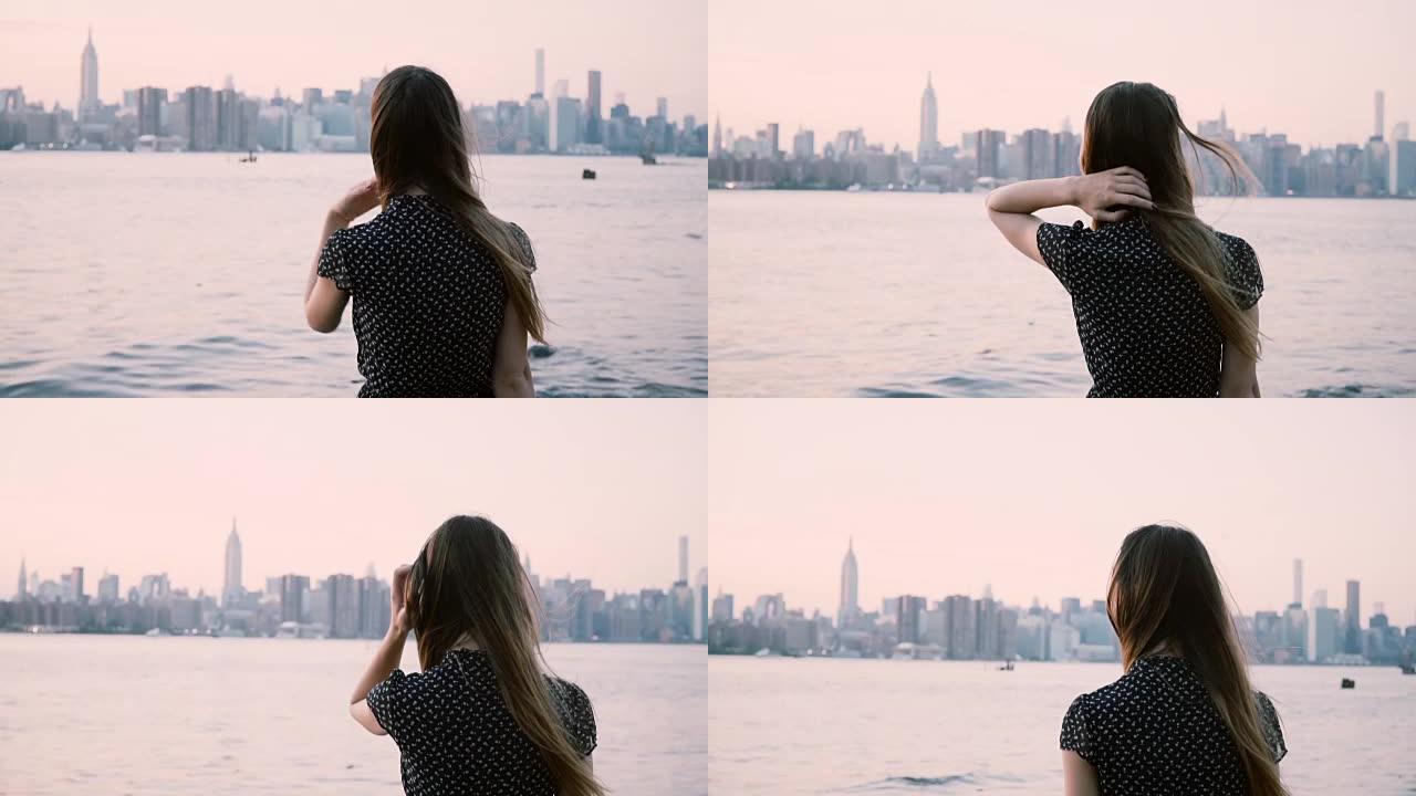 体贴的年轻高加索女孩，头发在风中吹，在纽约市河岸慢动作观看日落